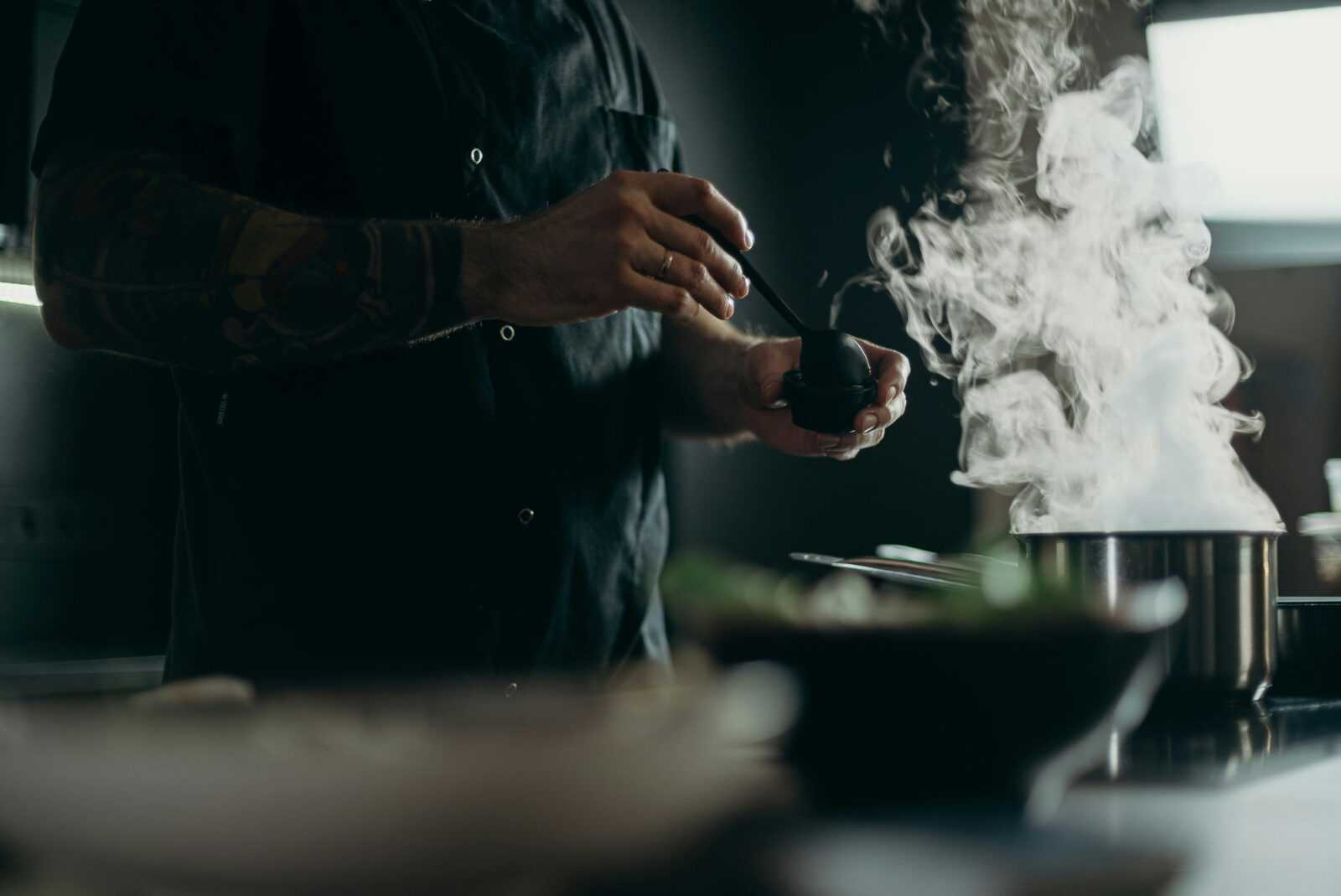 A chef carefully prepares a steamy dish in a professional kitchen setting.
