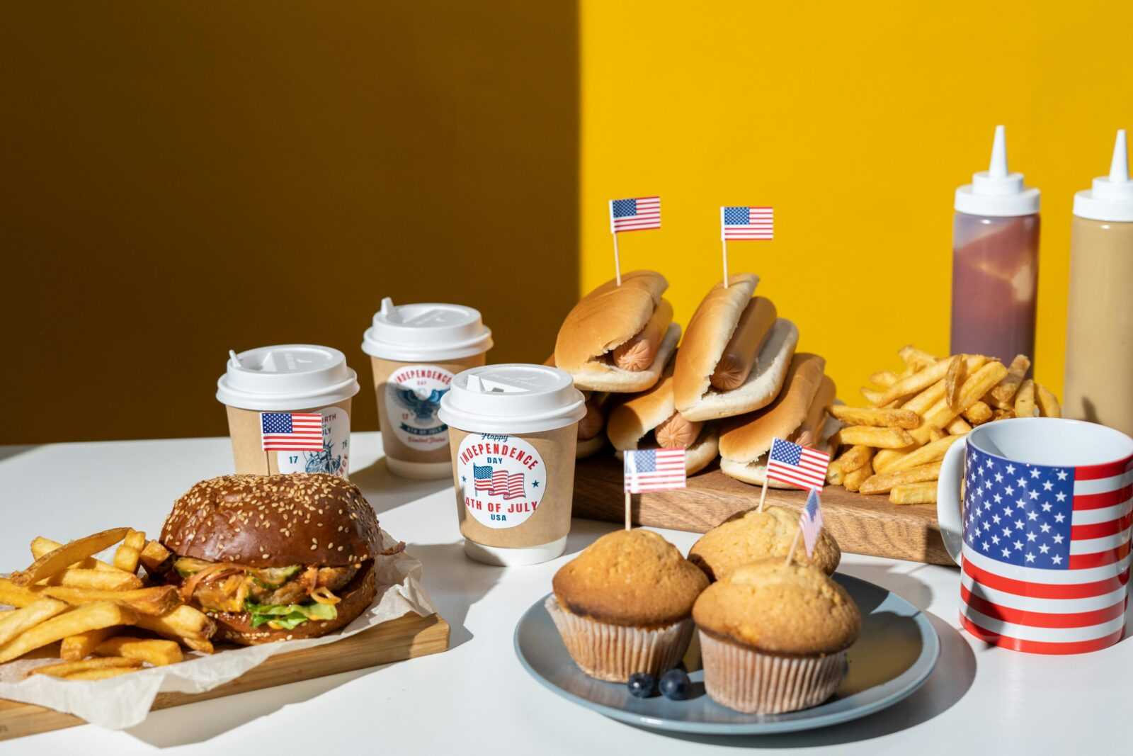 Festive 4th of July food setup with burgers, fries, muffins, and coffee cups.