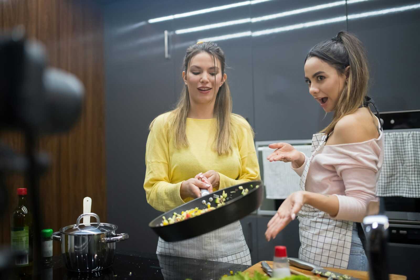 Two young women cooking together in a stylish kitchen, engaging in a fun culinary activity.
